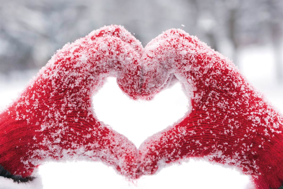 Hände formen ein Herz, die Person trägt rote Handschuhe und sind voller Schnee 