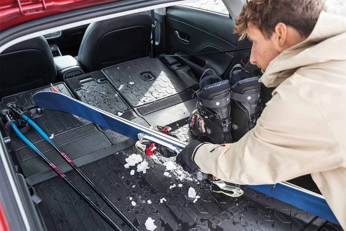 Formschalenmatte im Kofferraum, ein Mann lädt Skier ein