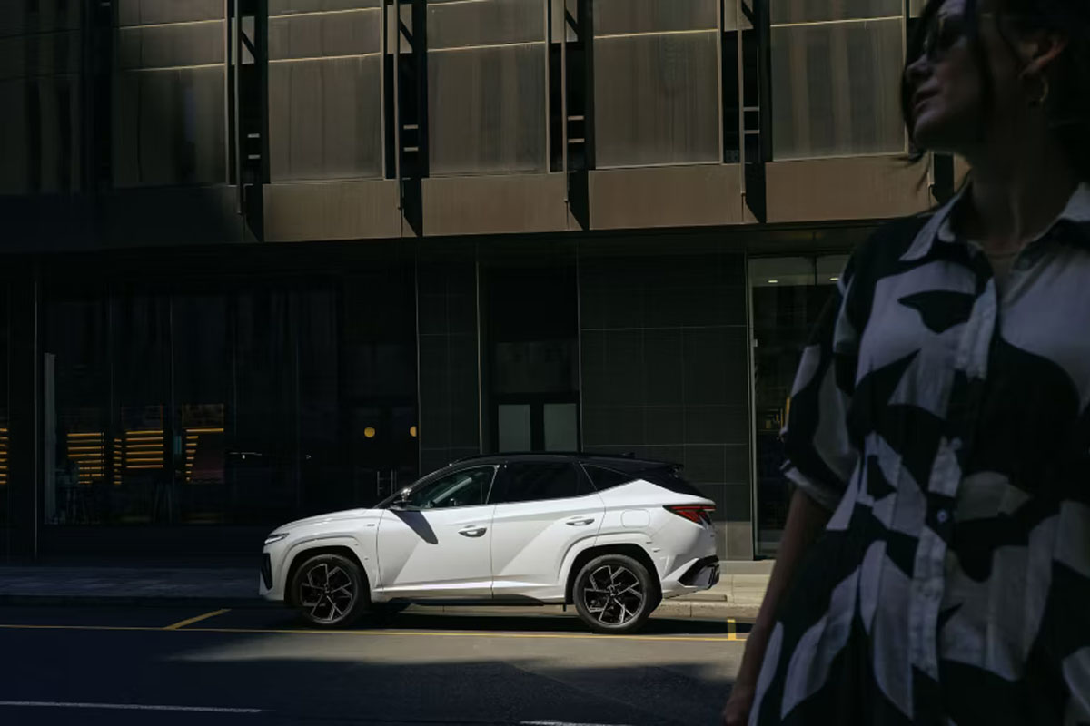 weißer Tucson vor einem Gebäude, rechts im Bild steht eine Frau.