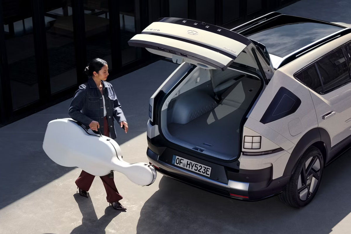 Eine Frau trägt eine Geige zum geöffneten Kofferraum