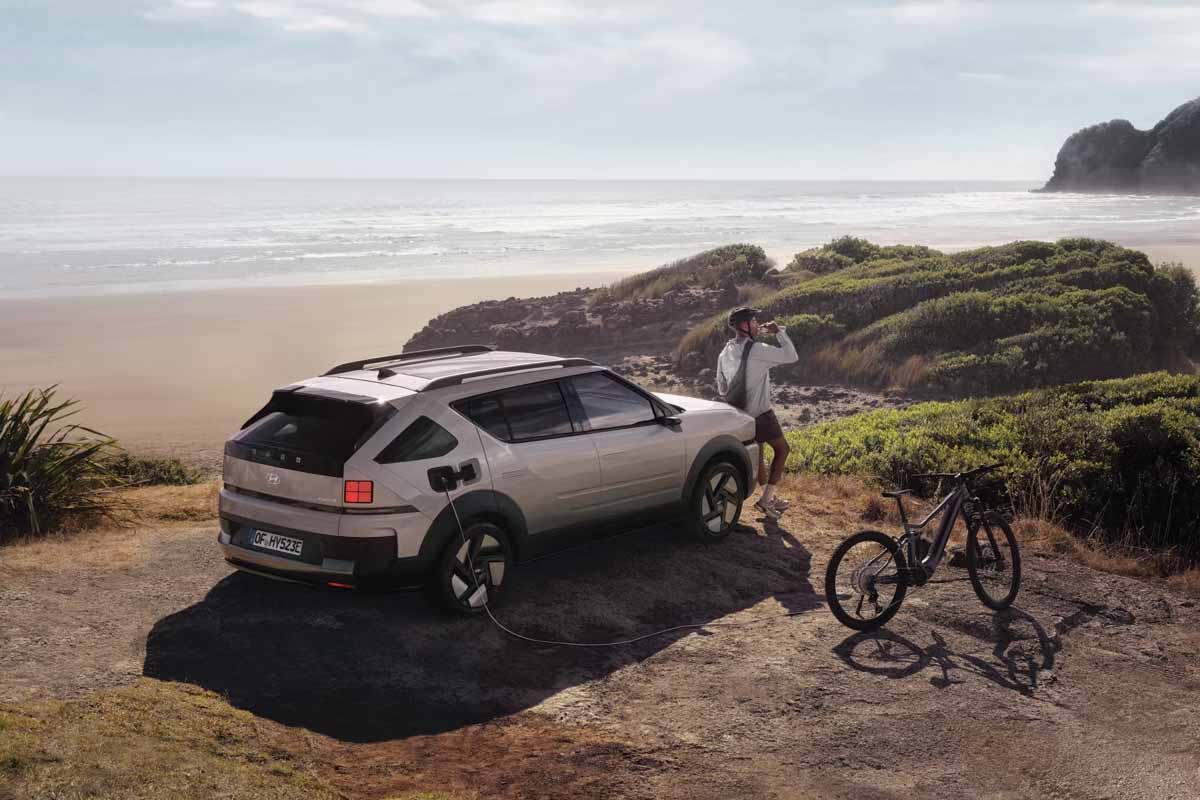 beiger NEXO am Strand, ein Mann lehnt daran, daneben steht ein Rad
